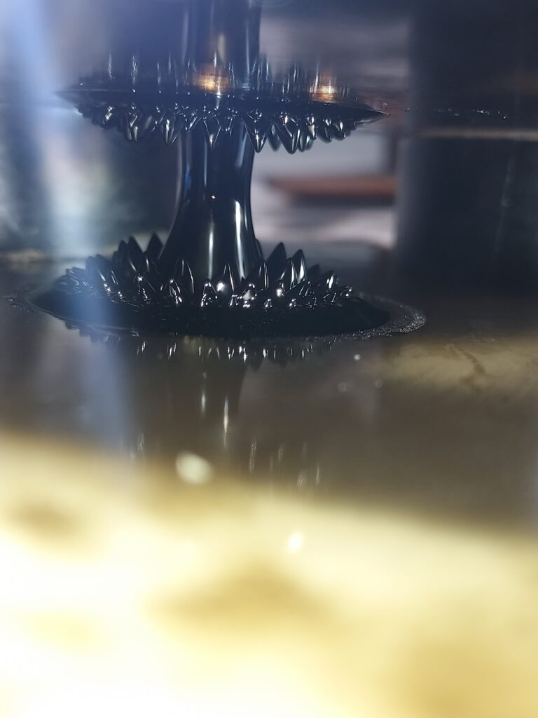 A tall, narrow ferrofluid bridge joins two glass panes, with spikes rising from below and hanging from above.